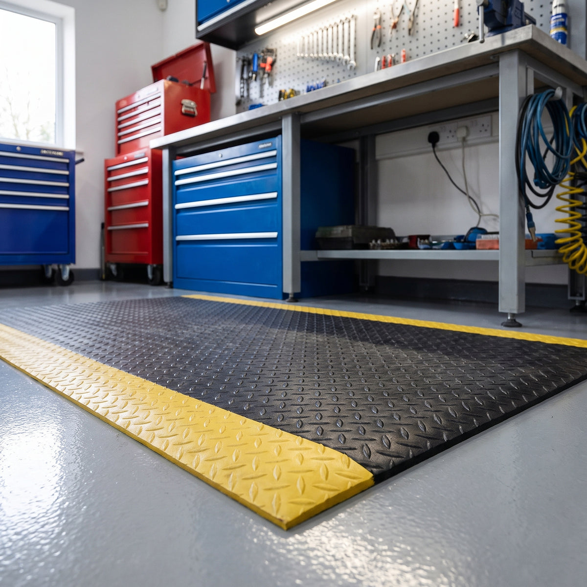 Black diamond plate anti fatigue mat with yellow safety border in front of a workshop bench