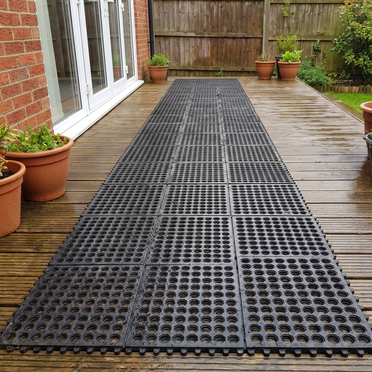 Interlocking anti-slip rubber mats installed as a walkway across wet garden decking by patio doors