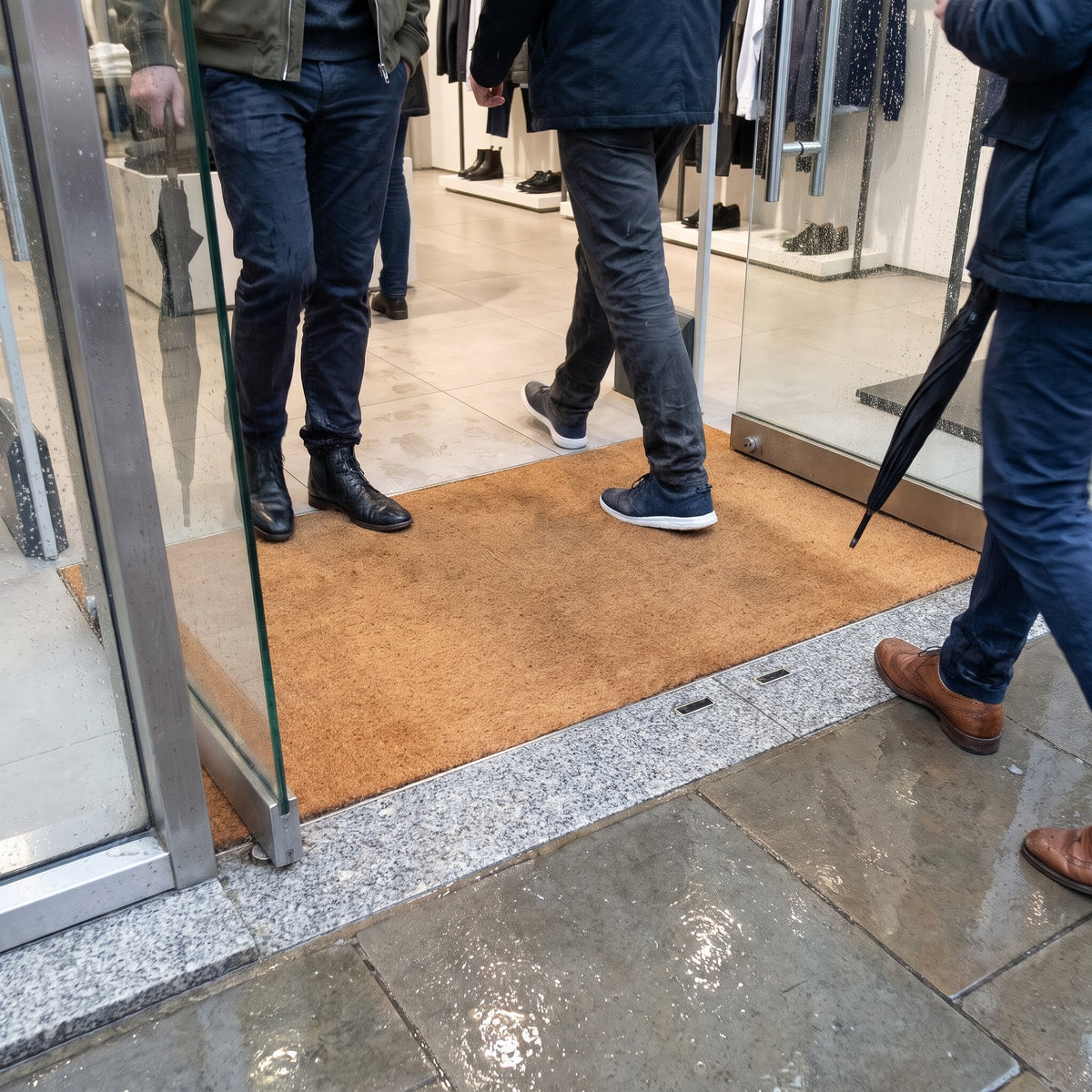 Customers stepping onto natural coir entrance matting in a shop doorway on a rainy day