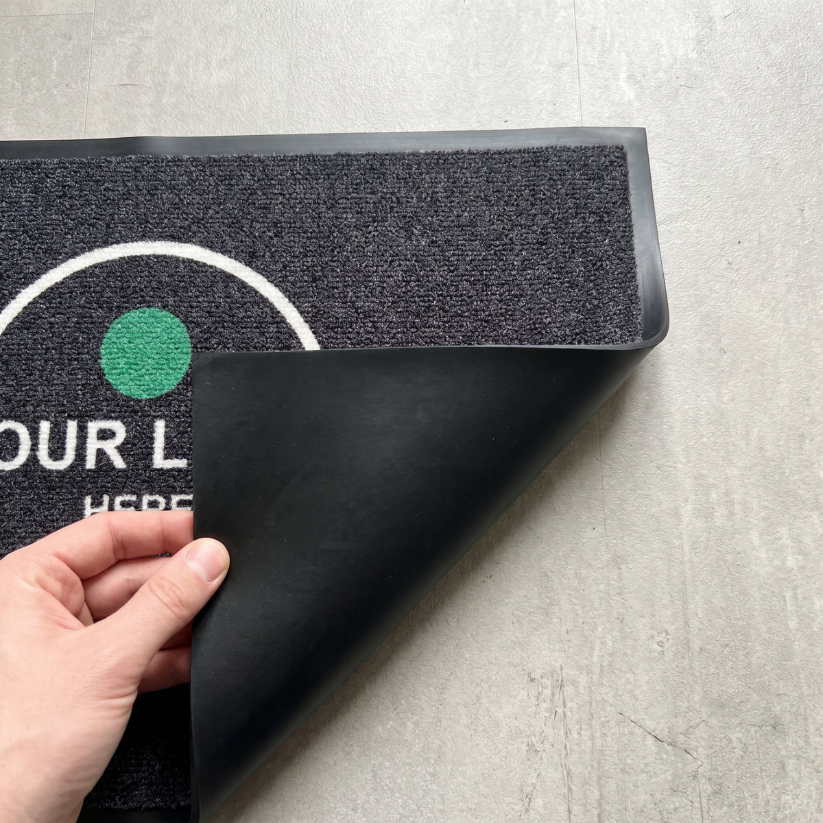 Close-up of logo mat corner showing printed pile and non-slip rubber backing