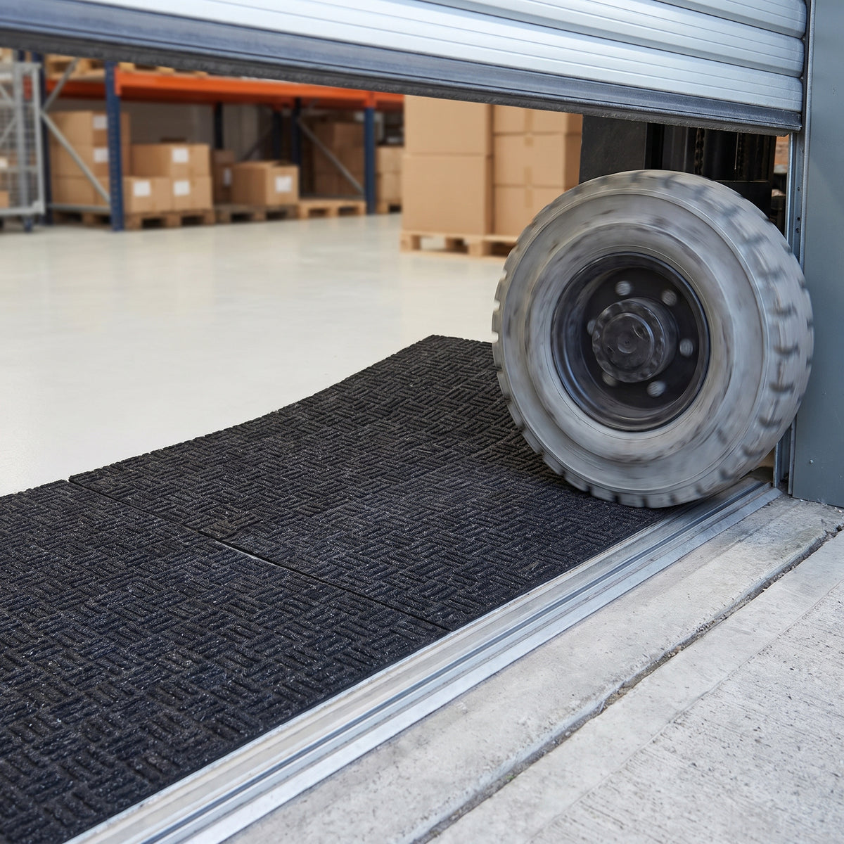 Forklift tyre rolling onto charcoal forklift mat tiles laid across a warehouse roller-shutter doorway