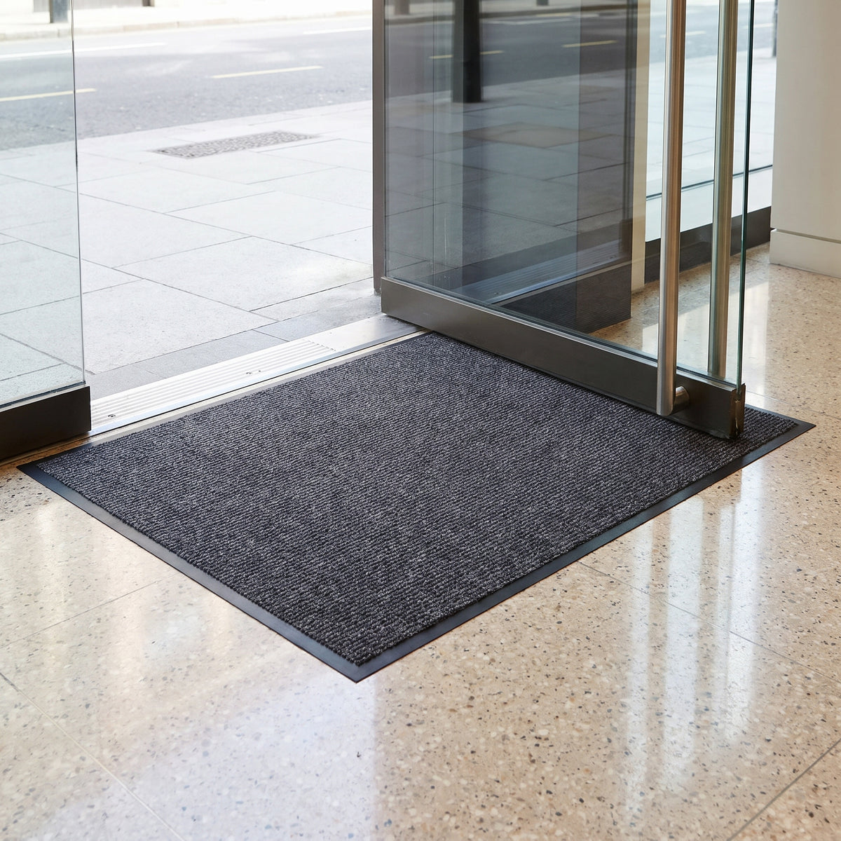7mm low-profile entrance mat sitting flat under the swing of a glass shop door
