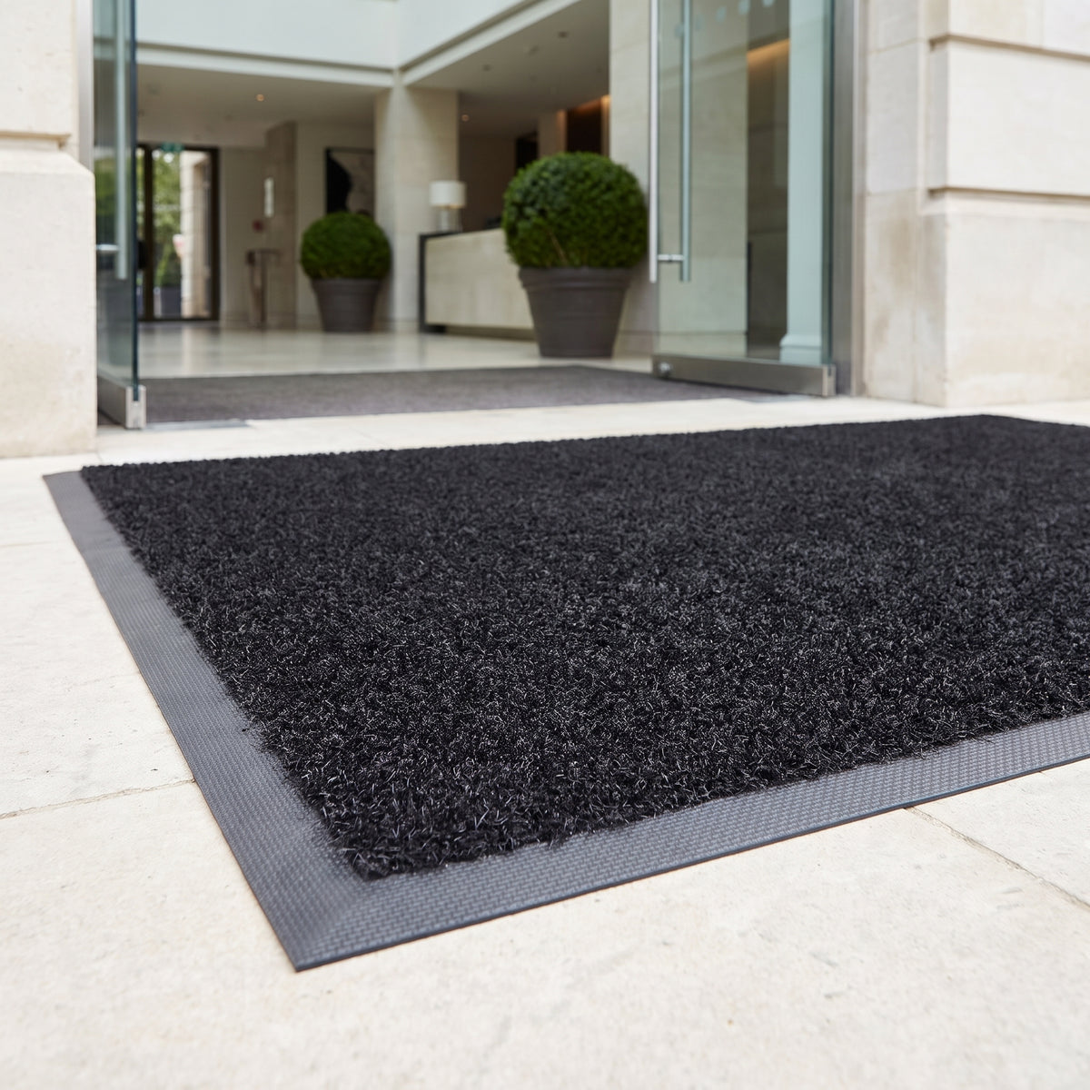 Black heavy-duty outdoor brush entrance mat with rubber border outside a luxury hotel entrance