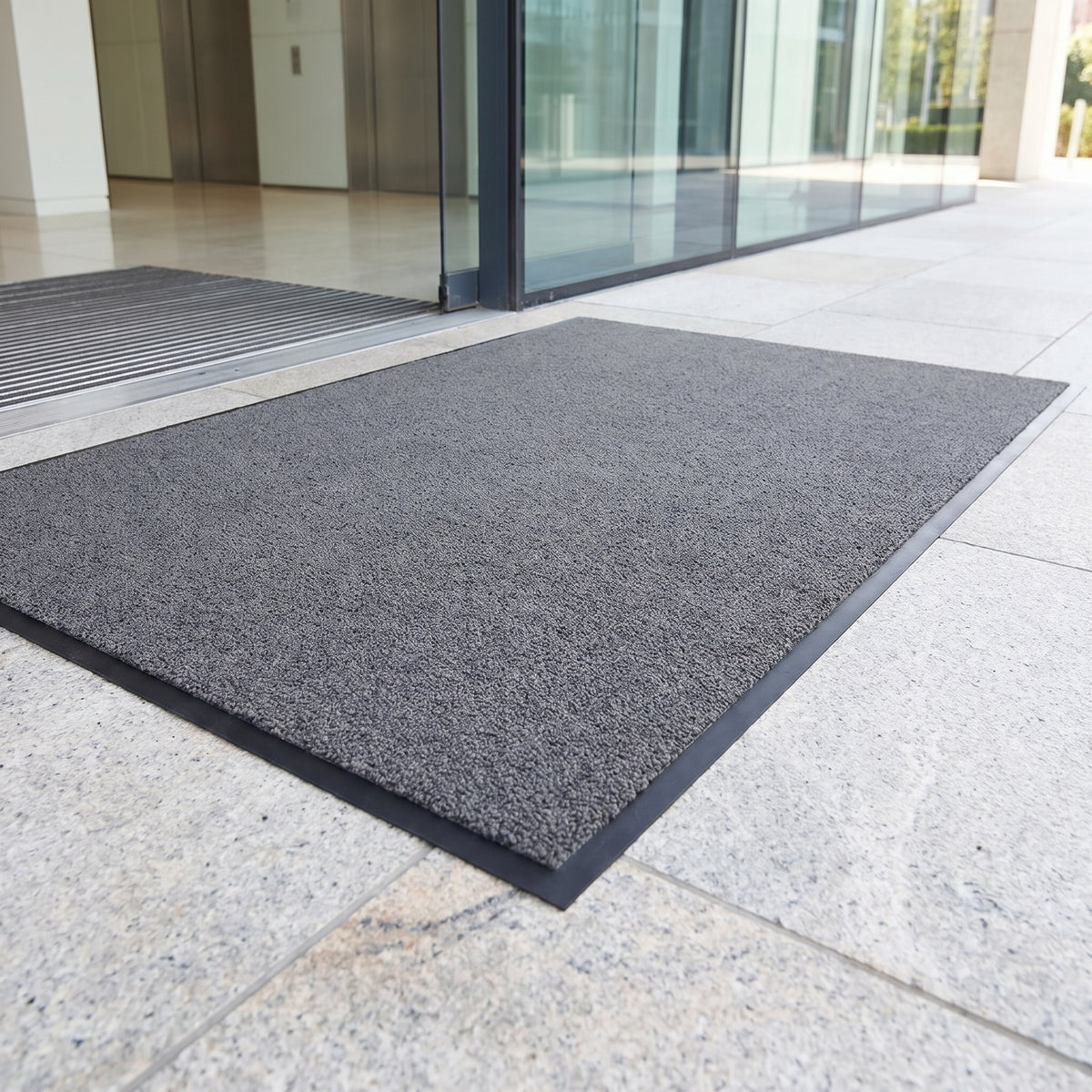 Dark grey outdoor brush entrance mat on granite paving outside a corporate headquarters