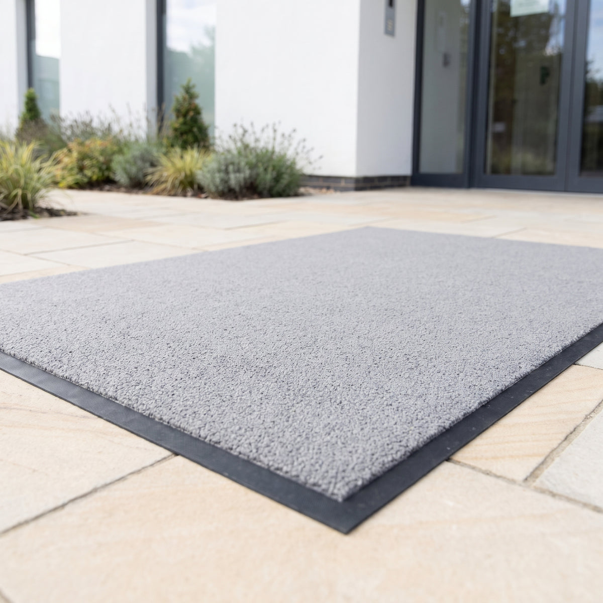 Light grey outdoor brush entrance mat on sandstone paving at a private clinic entrance