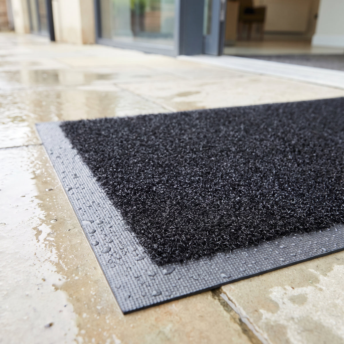 Close-up of outdoor brush mat pile and rubber border with rain beading on wet paving