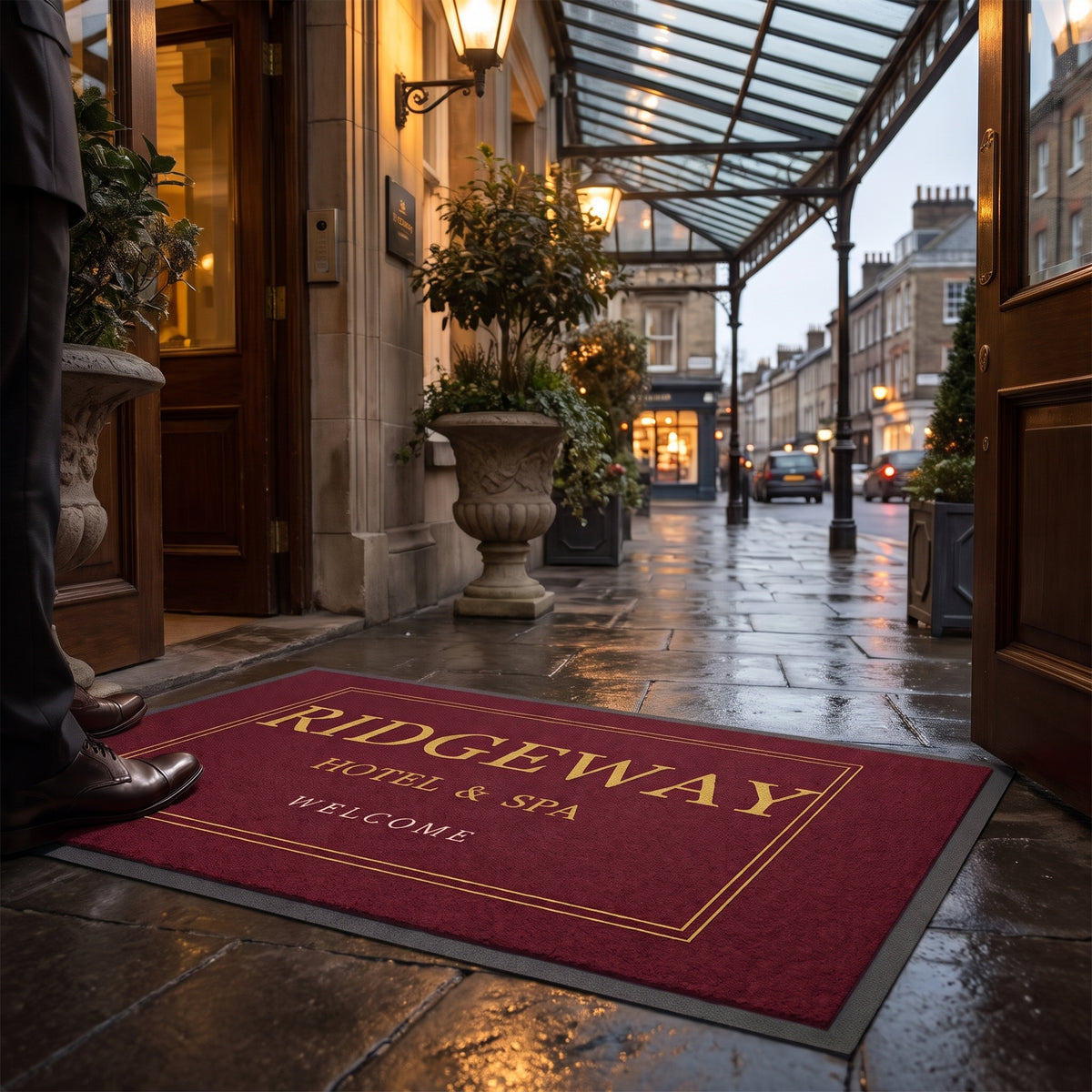 Example design: burgundy and gold outdoor logo mat on the stone forecourt of a hotel entrance at dusk