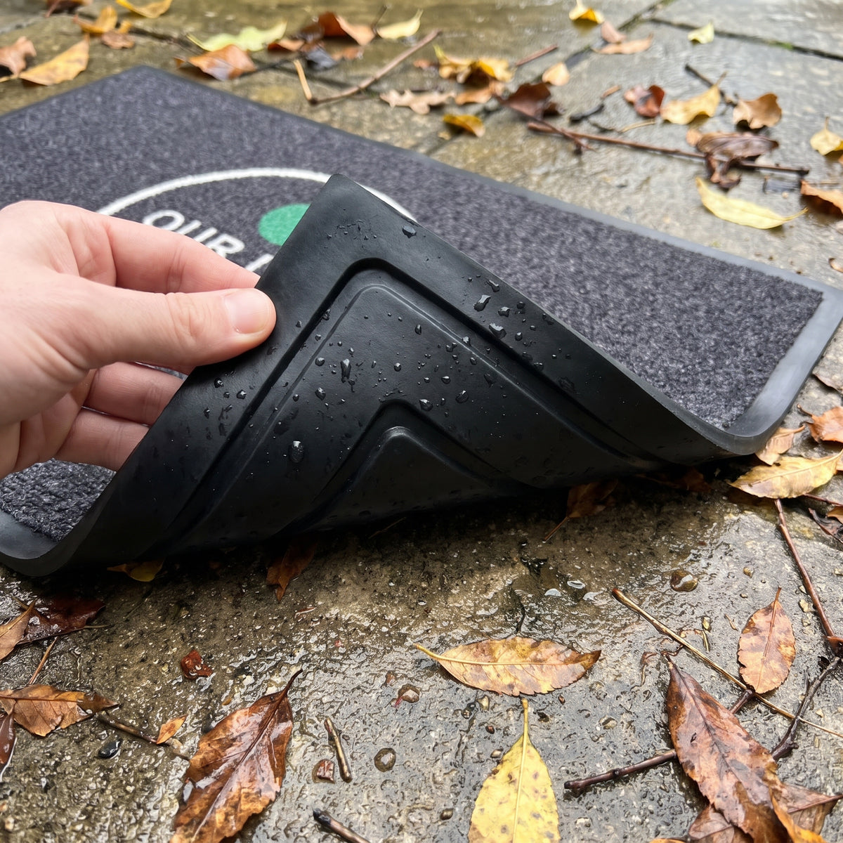 Corner of an outdoor logo mat lifted to show the nitrile rubber backing with moulded drainage channels