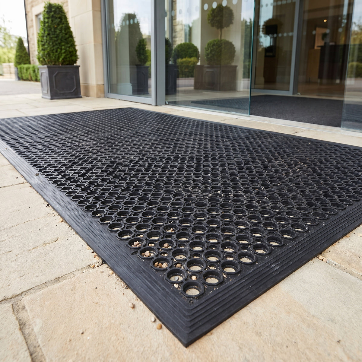 Black rubber drainage entrance mat with ramped edges outside a luxury hotel entrance in daylight