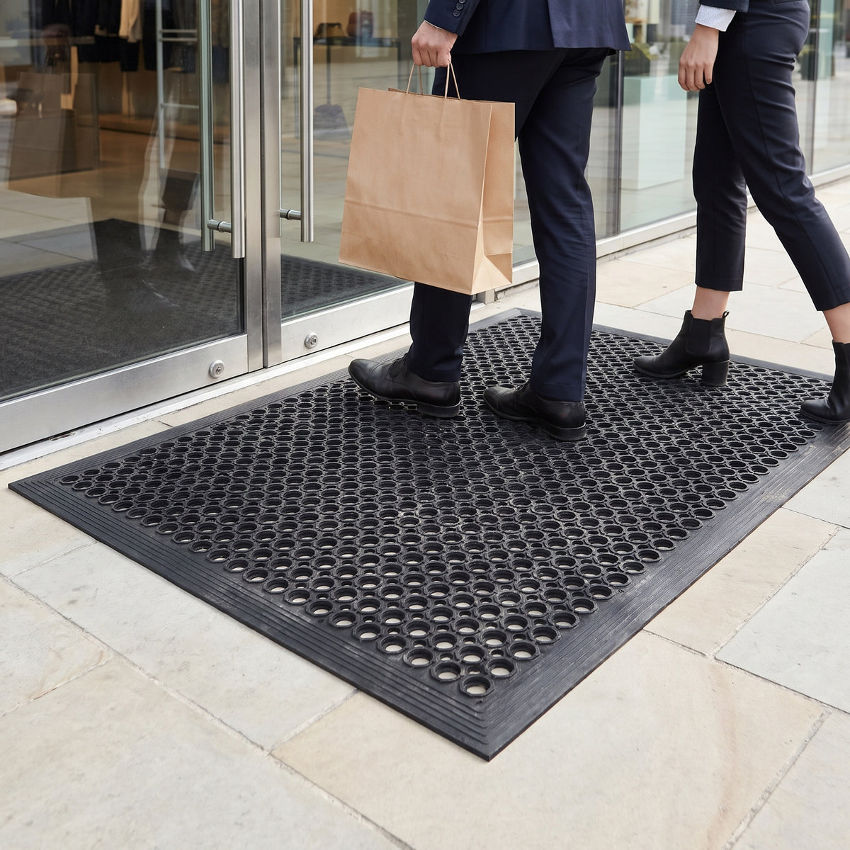 Shoppers stepping across an outdoor rubber drainage mat at a retail store entrance