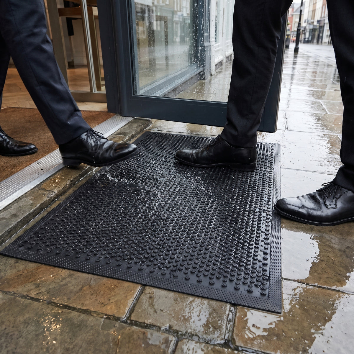 Outdoor rubber scraper mat cleaning shoes at a shop doorway on a rainy day